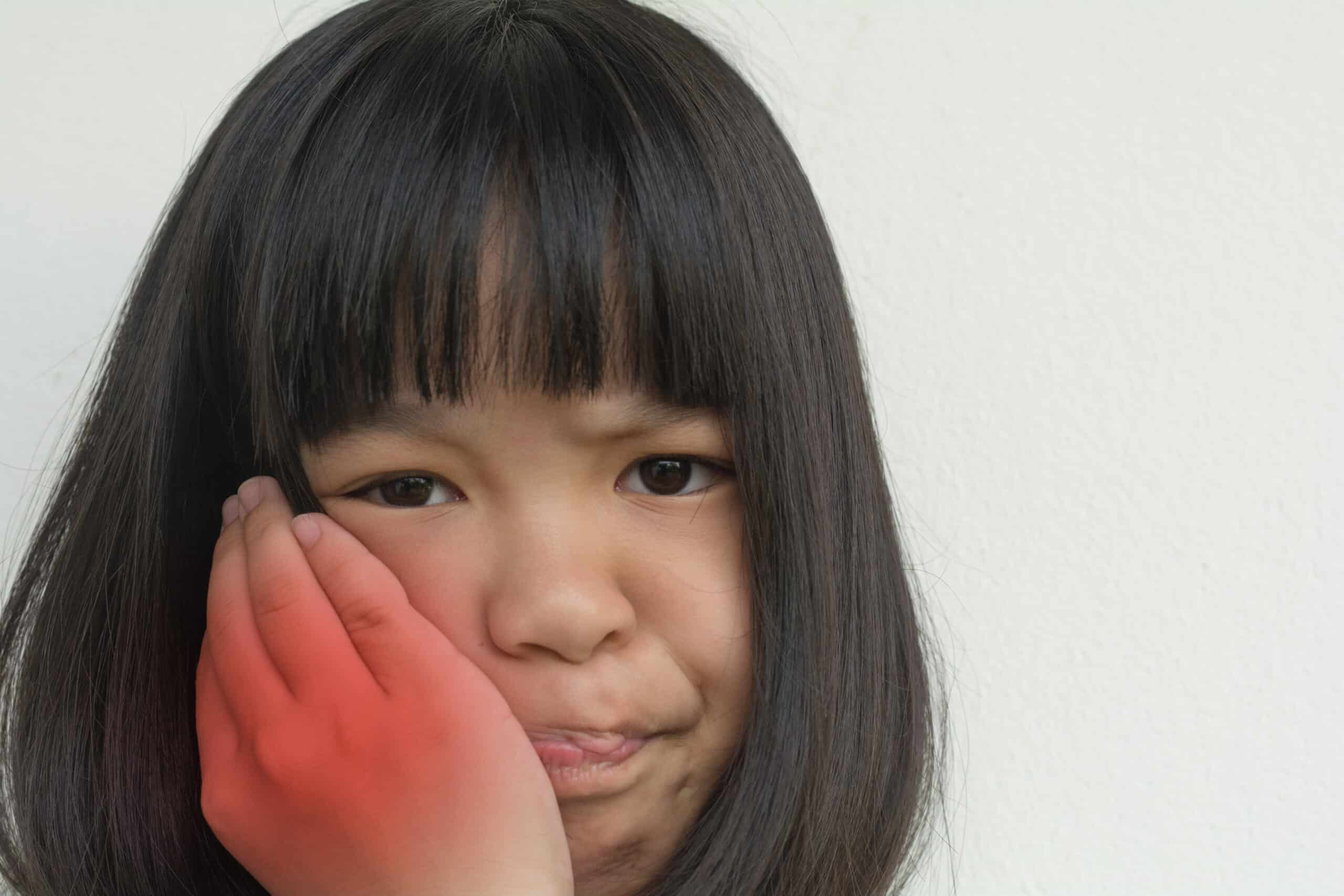 A younger girl cupping one side of her mouth with red coloring highlighting the painful area of her jaw.