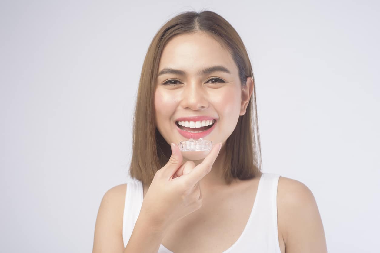 Young smiling woman holding Invisalign braces over white background studio