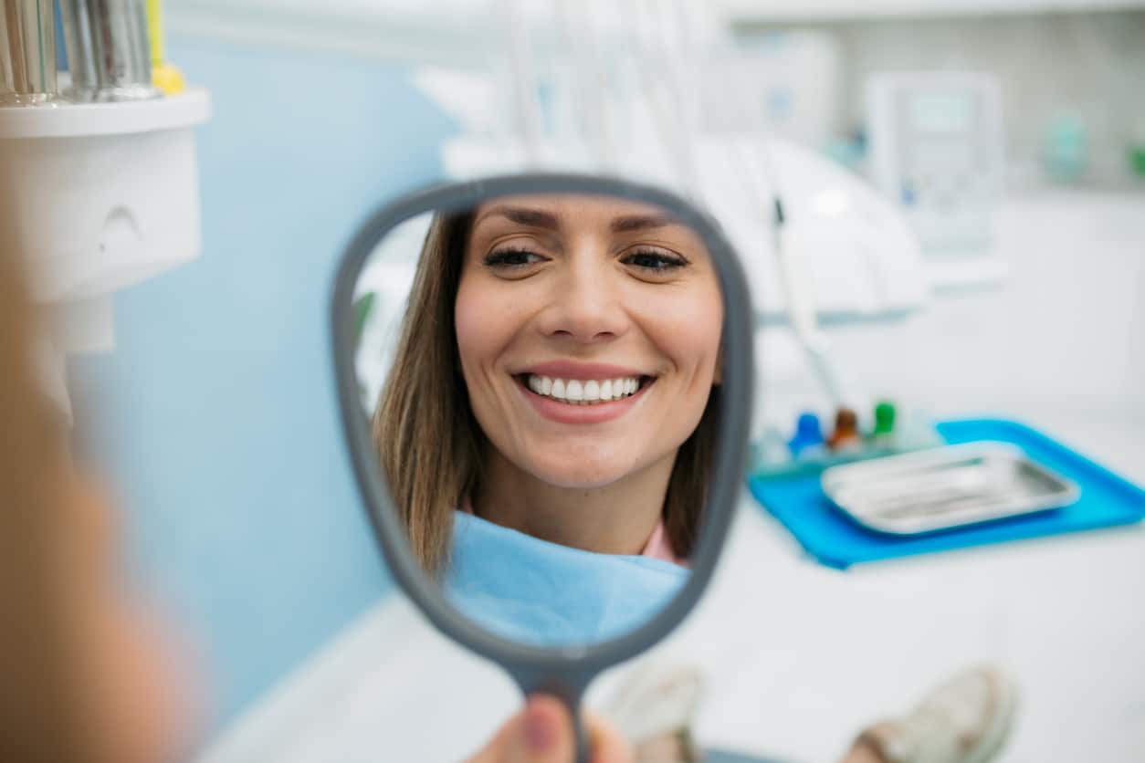 A happy woman looking at herself in the handheld mirror.