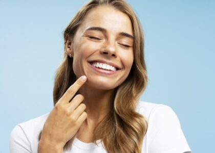 A woman with long, dirty-blonde hair points to her smile after following the essential steps to preventing tooth loss.