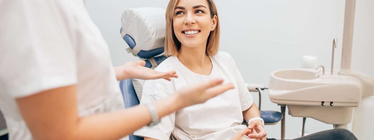 a person sitting in a room A woman seated in a dental chair speaks with her dentist about managing dental anxiety.