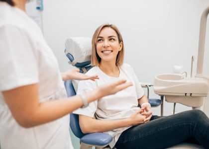 A woman seated in a dental chair speaks with her dentist about managing dental anxiety.