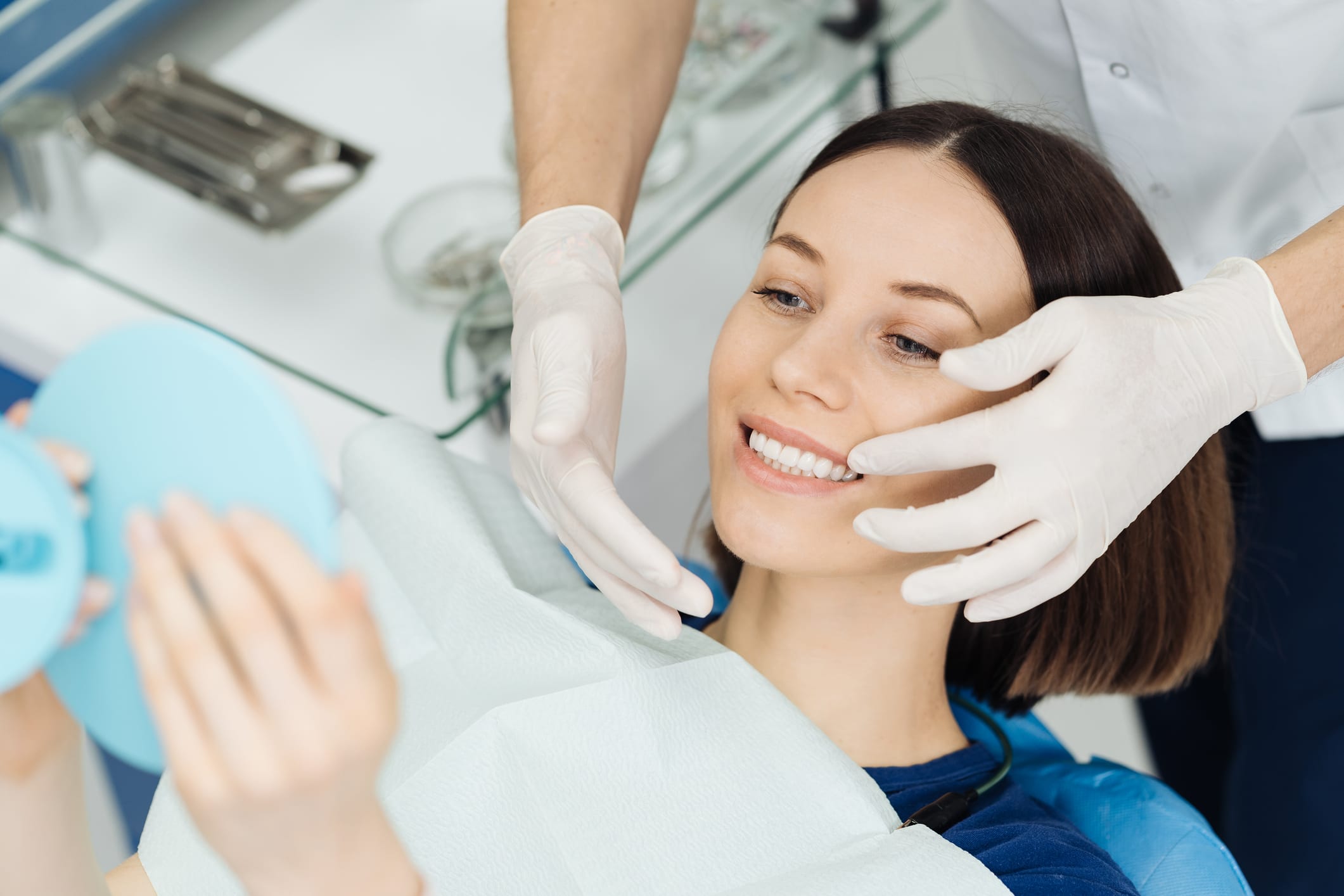 A woman with shoulder-length brown hair sits in a dental chair and smiles after undergoing advanced cosmetic dental work.