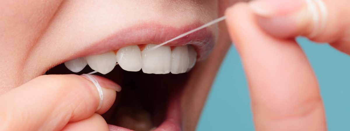 A woman flosses her teeth, showcasing her commitment to oral health and keeping her cosmetic dental work in the best condition.