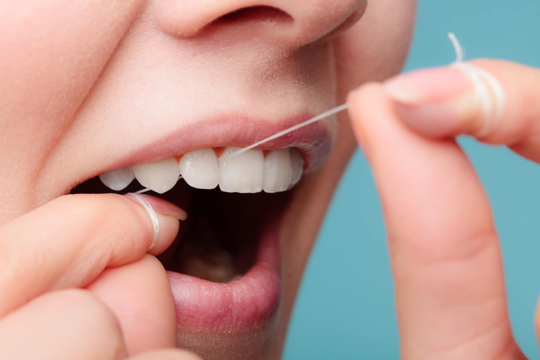 A woman flosses her teeth, showcasing her commitment to oral health and keeping her cosmetic dental work in the best condition.