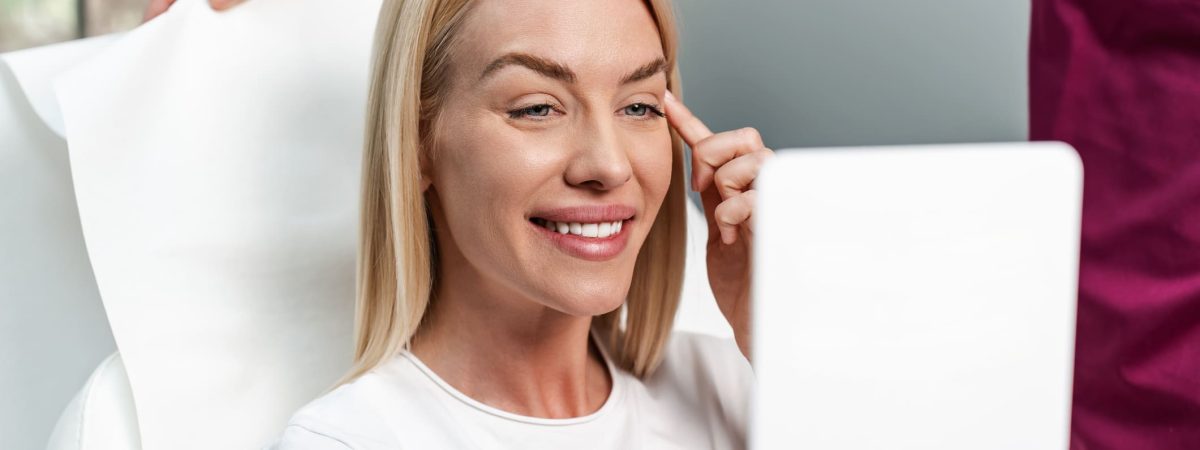 a woman in a white shirt A woman sitting in a dental chair smiles, happy with her new look after getting botox® injections for the holiday season.