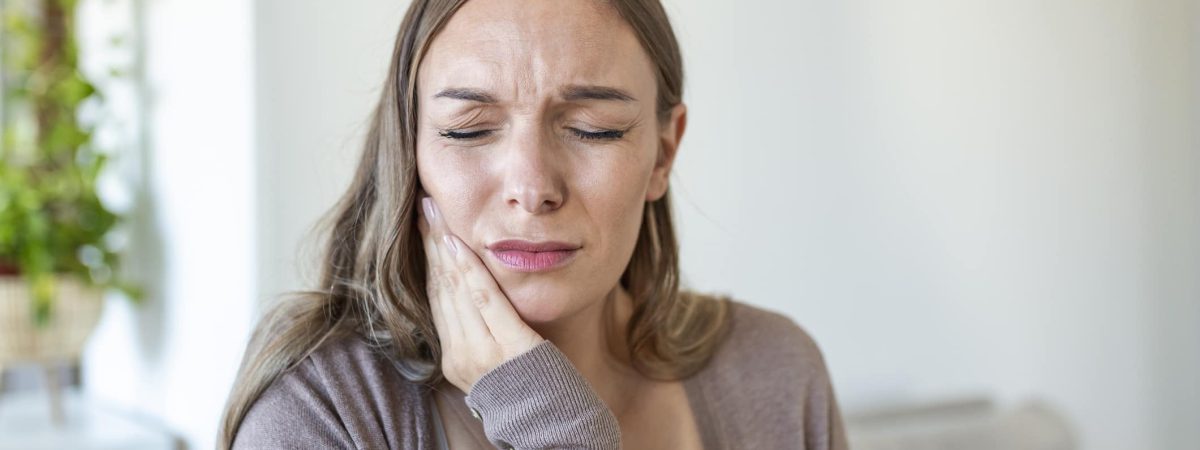 a woman smiling for the camera A woman sitting on a couch holds her jaw in pain and considers seeking professional TMJ treatment.