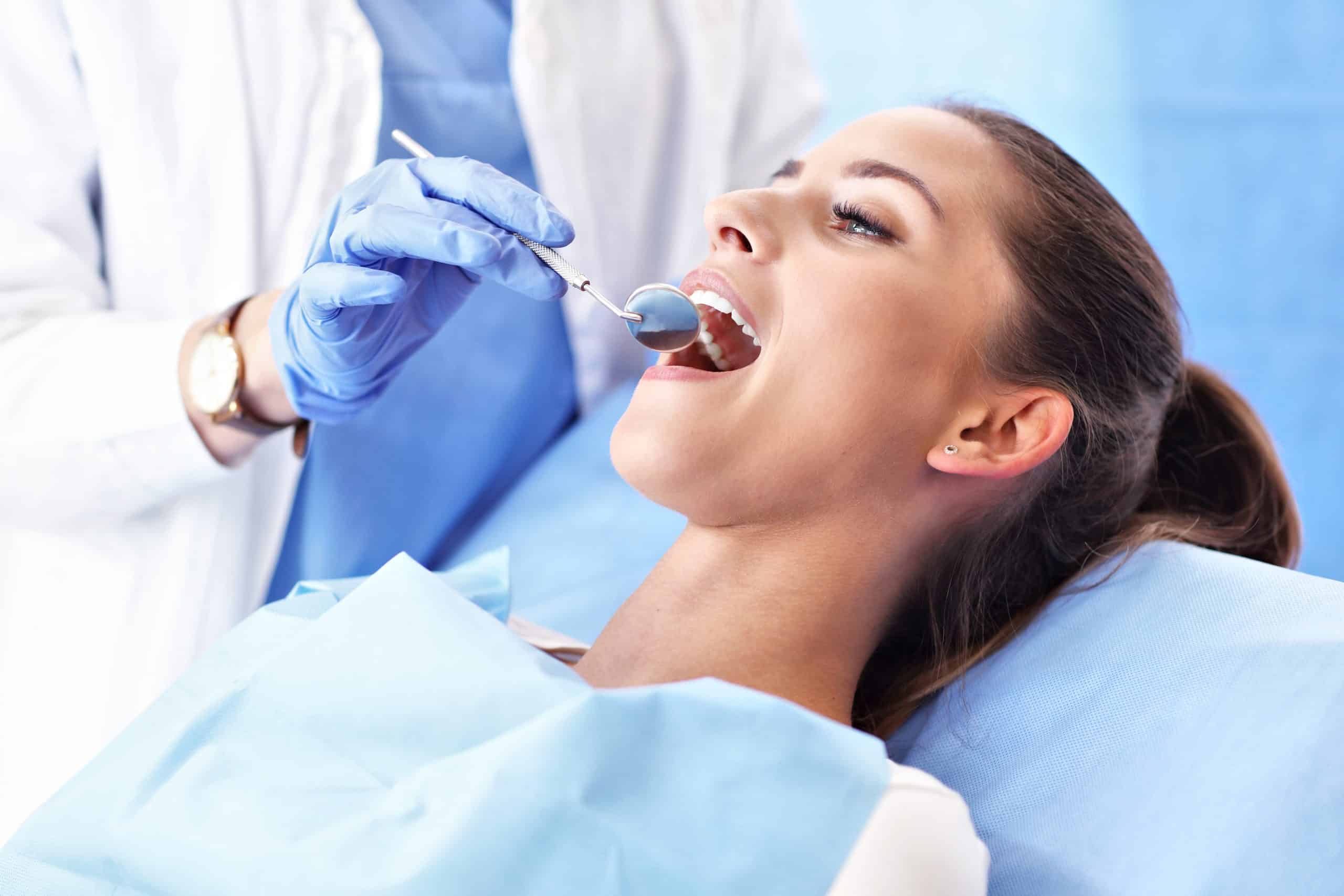 young woman having her teeth examined by a doctor in blue gloves